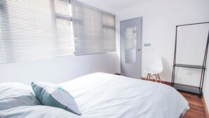 A bedroom with a bed, a door, a chair, and a window with blinds. - Urbana Hostel (Bogotá)