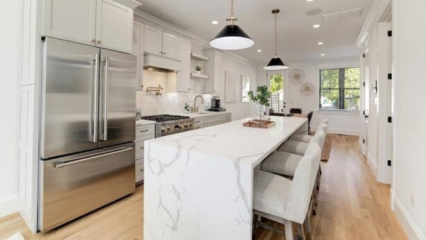 A modern kitchen with stainless steel appliances, a marble island, and a dining area with bar stools. - Gorgeous Newly Built 3BR Home in Alexandria (Alexandria)