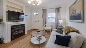 Ein Wohnzimmer mit Kamin, Fernseher, rundem Couchtisch, Sofa und einem Gemälde an der Wand.