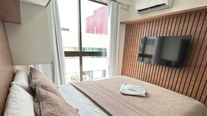 Una habitación de hotel moderna con una cama grande, un televisor de pantalla plana montado en la pared y un equipo de aire acondicionado encima.