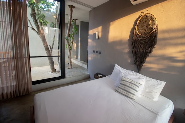 A bedroom with a large bed, a wall-mounted dreamcatcher, and a view of a tree outside.