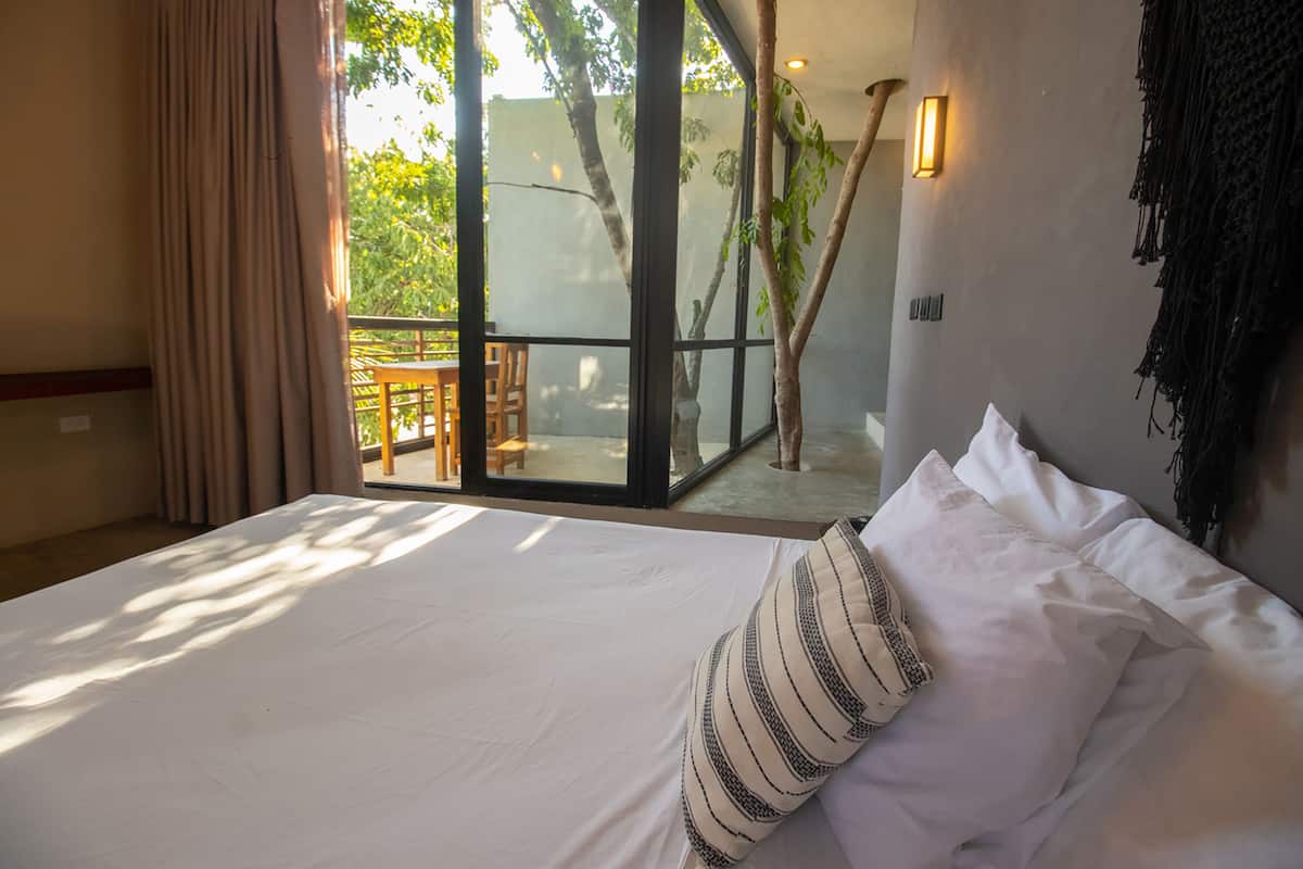 Habitación de hotel con una cama grande, vistas al exterior y un balcón con mesa y sillas.