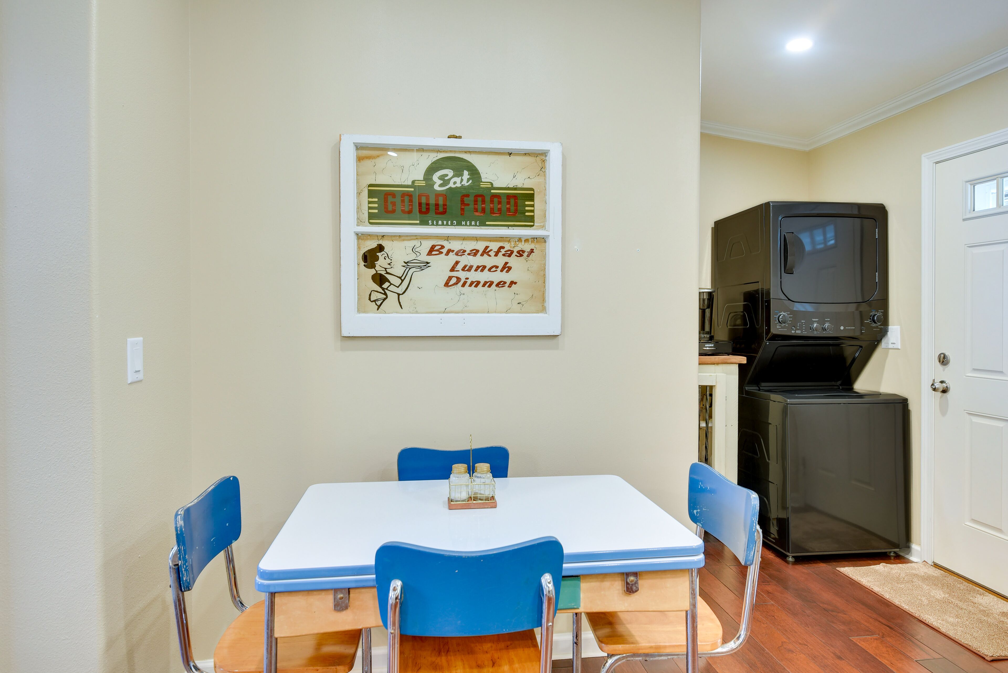 A dining area with a table and chairs, a vintage sign above the table, and a microwave in the background.