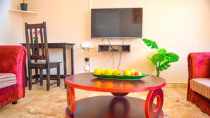 A living room with a round wooden coffee table, a flat-screen TV mounted on the wall, a potted plant, and two red upholstered chairs. - Fantastic Location, 1-bed Apartment in Harare (Harare)