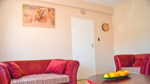 A living room with a red sofa, a dining table with fruit, a door, and a clock on the wall. - Fantastic Location, 1-bed Apartment in Harare (Harare)