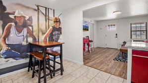 A modern kitchen with a red refrigerator, a wooden dining table, and a kitchen island. - Route 66 Downtown Burgundy Bungalow w/Fenced Yard, AC, W/D, 3 Smart TVs, Wi-Fi (Williams)