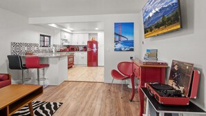A modern kitchen with white cabinets, a red refrigerator, and a dining area with red chairs and a wooden table. - Route 66 Downtown Burgundy Bungalow w/Fenced Yard, AC, W/D, 3 Smart TVs, Wi-Fi (Williams)