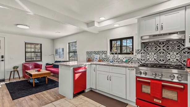 A modern kitchen with white cabinets, a red dishwasher, and a stainless steel stove. - Route 66 Downtown Burgundy Bungalow w/Fenced Yard, AC, W/D, 3 Smart TVs, Wi-Fi (Williams)