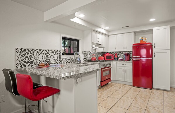 Una cocina con armarios blancos, un refrigerador rojo, una estufa roja y un salpicadero con estampado blanco y negro.
