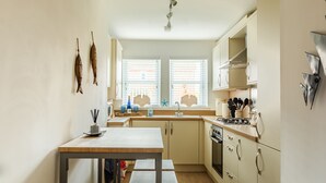 A compact kitchen with a wooden table, two windows with blinds, and a built-in oven.