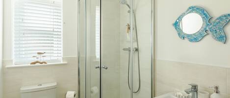 Ein Badezimmer mit Duschkabine, Toilette, Waschbecken mit Pflegeprodukten und Fenster mit Jalousien.