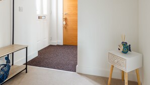 A hallway with a wooden door, a heart-shaped wall decoration, a hanging light fixture, and a small table with a decorative item.
