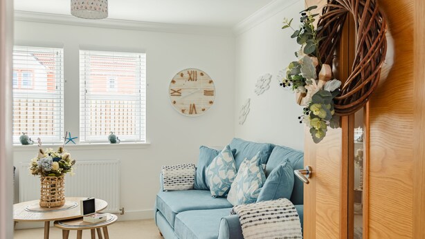 A cozy living room with a blue sofa, a round wooden clock, and a wicker table with a vase of flowers.