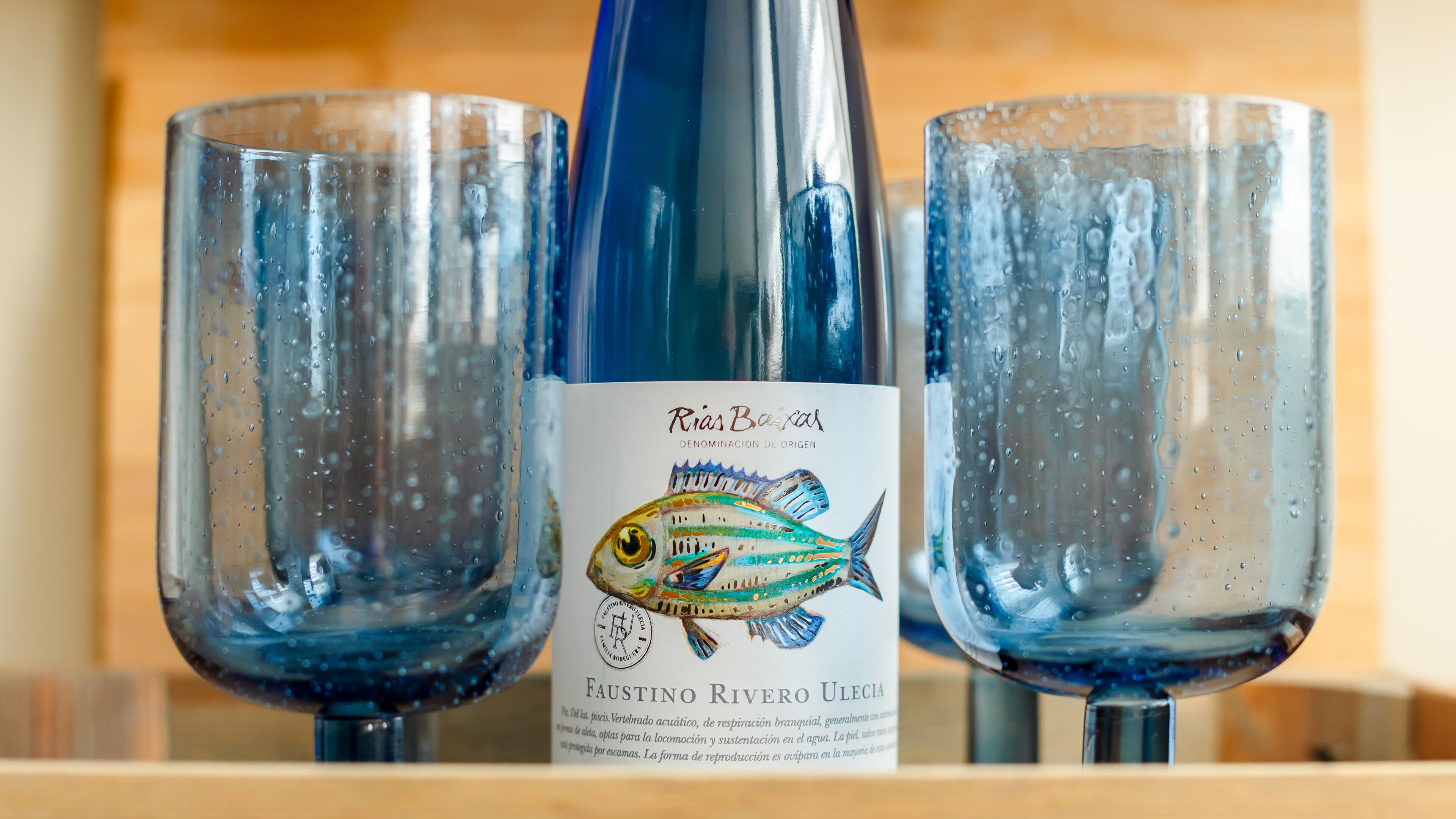 Une bouteille de vin de Rias Baixas, dont l’étiquette présente une illustration de poisson, est placée entre deux verres.