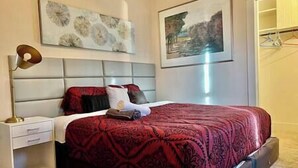 Ein Schlafzimmer mit einem großen Bett, einem Nachttisch, einer Lampe und zwei gerahmten Bildern an der Wand.