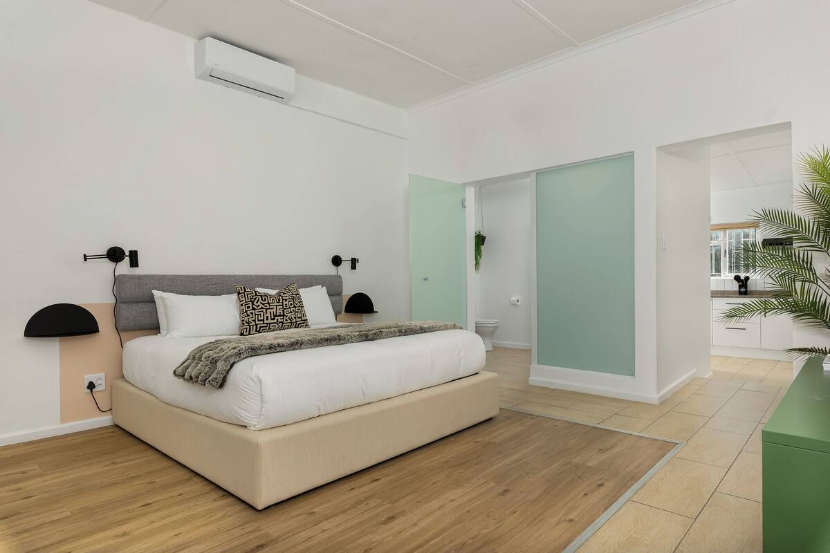 A modern bedroom with a large bed, bedside lamps, and a view of the outside.