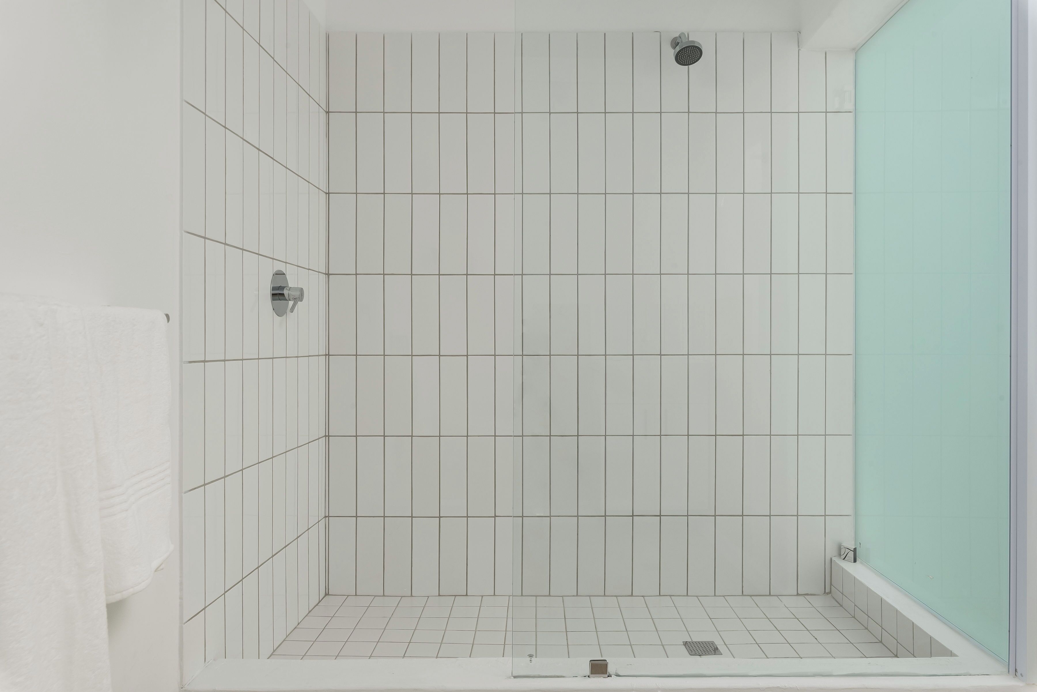 Un baño con paredes y suelo de baldosas blancas, zona de ducha y ba ñera.