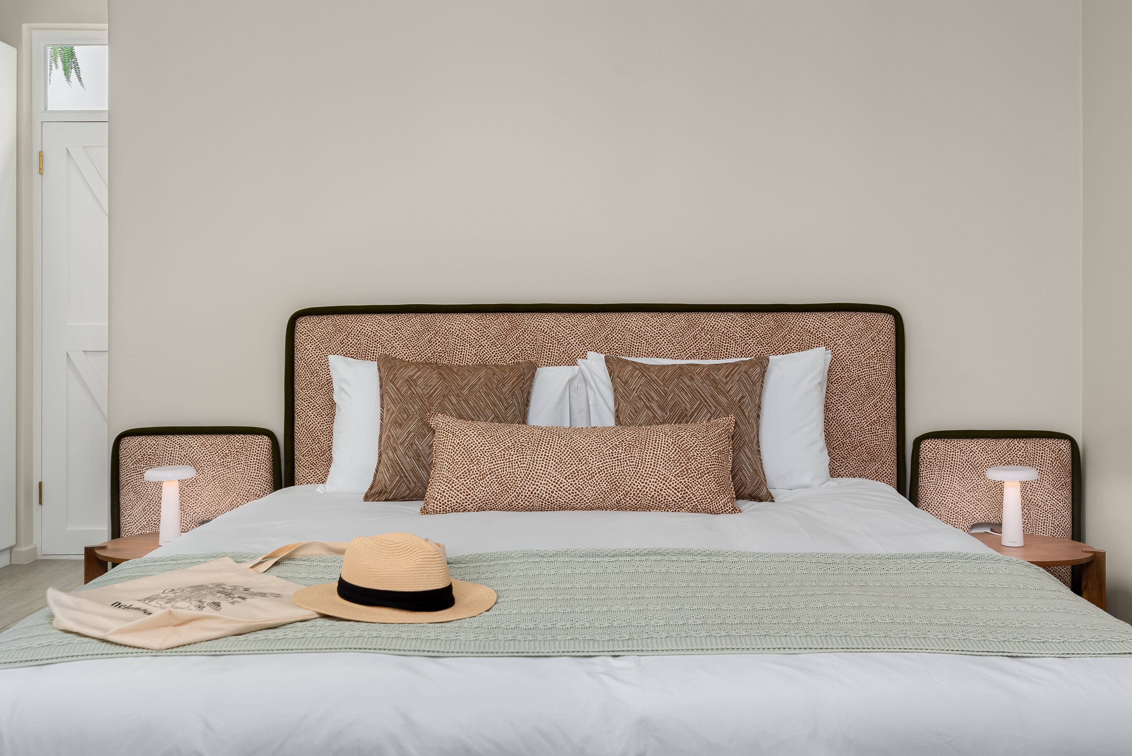 Ein ordentlich gemachtes Bett mit gemusterten Kissen, einem Hut und einer Decke auf einer grünen Bettdecke.