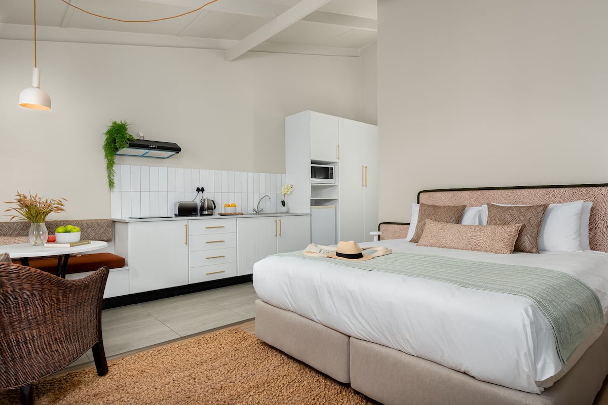 A modern bedroom with a large bed, a dining area with a table and chairs, and a kitchenette with cabinets and a microwave.