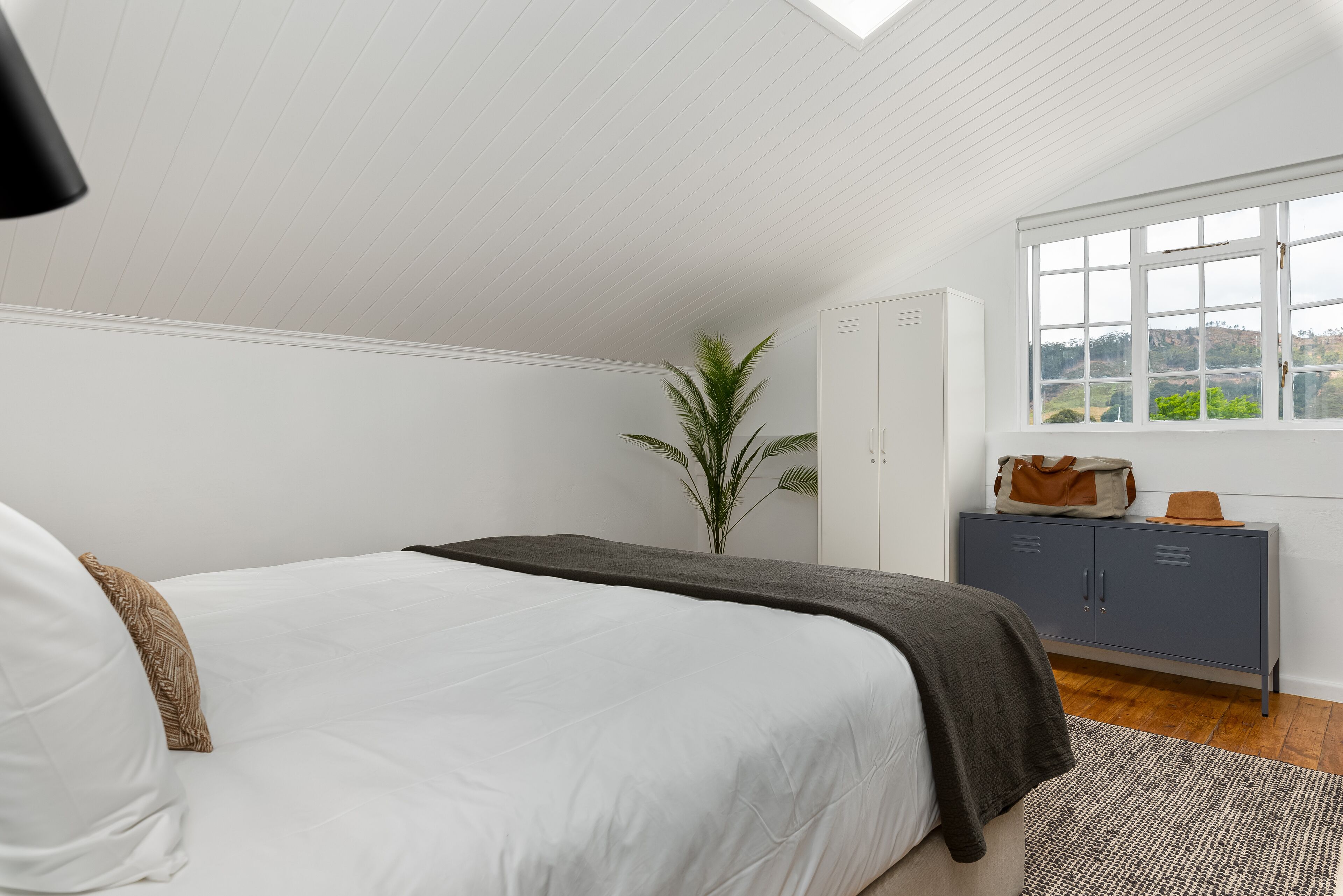 Un dormitorio con cama, armario, ventana con vistas y una planta.