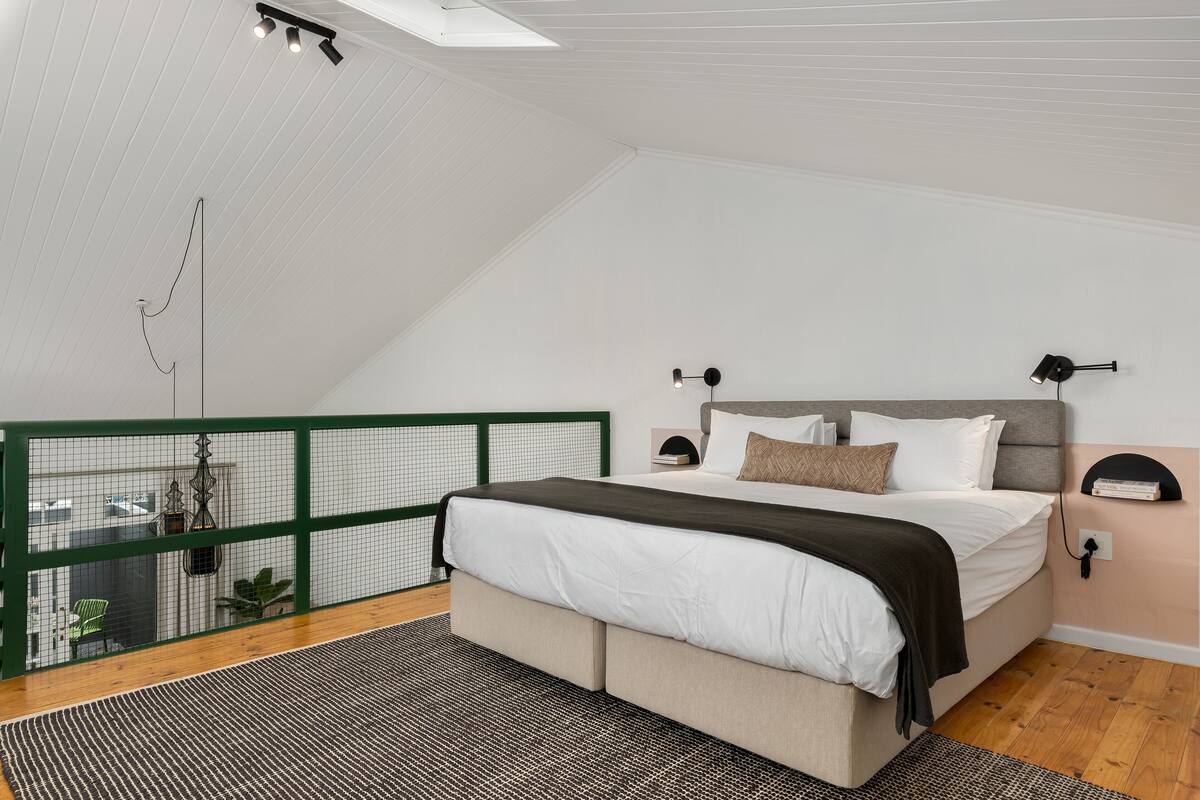 A bedroom with a bed, a green railing, a hanging light fixture, and a small plant.
