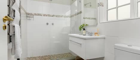 A modern bathroom with a glass shower enclosure, a white sink with a mirror above it, and a window providing natural light.