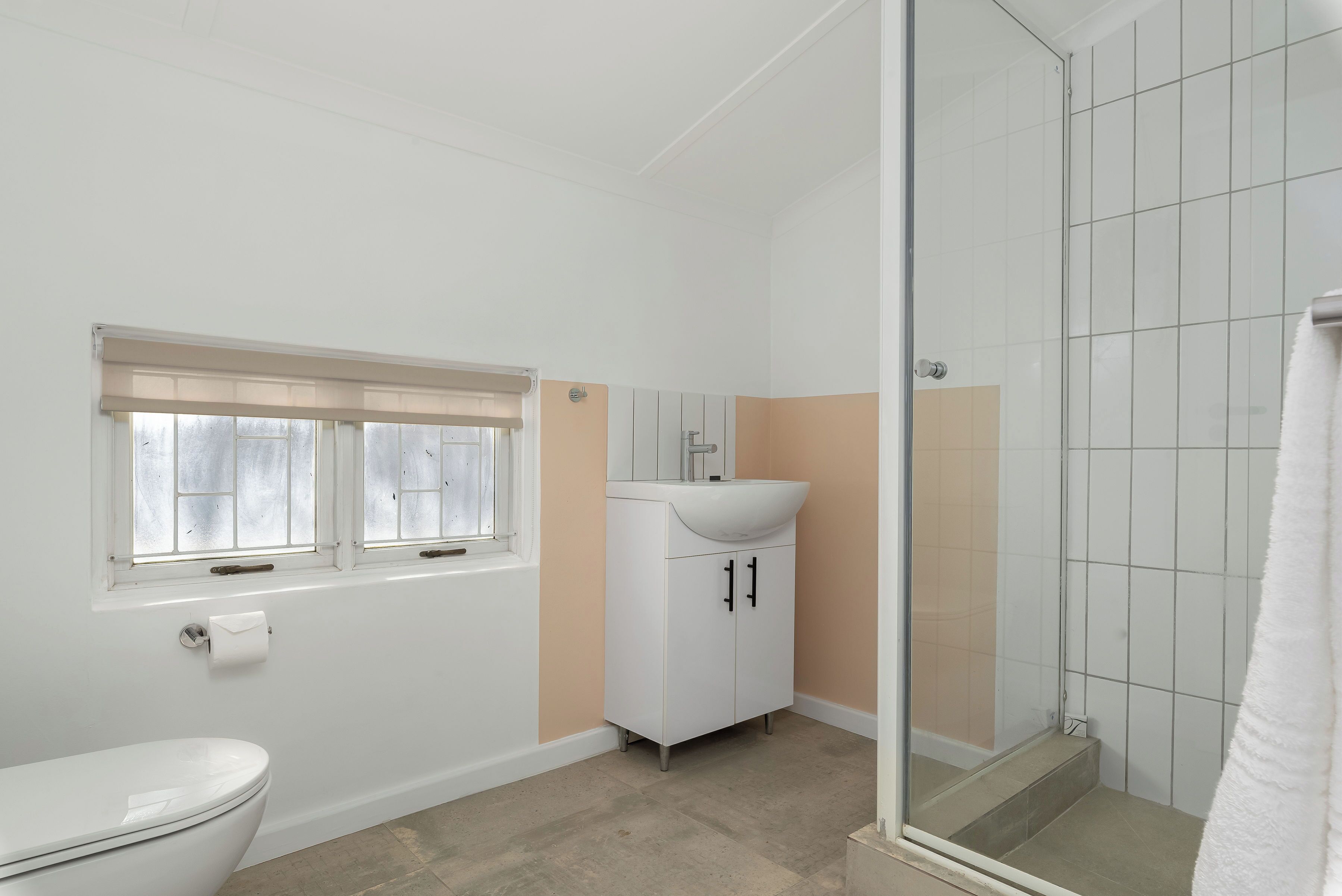 A bathroom with a toilet, a sink, a shower, and a window with blinds.