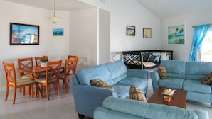 Un soggiorno con un divano blu, un tavolo da pranzo in legno, sedie e una ventola a soffitto.
