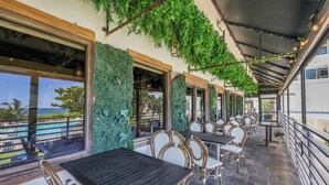 An outdoor patio with tables and chairs, a view of the ocean, and a covered area with hanging lights.
