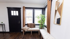 A room with a black door, a bench, a cushioned seat, a potted plant, and a geometric wall decoration. - Flagship Park - 10 Mins to Everything! (Kansas City)