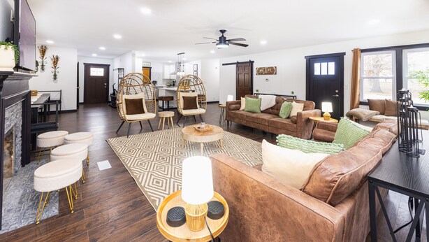 A spacious living room with a brown leather sofa, two wicker chairs, a wooden coffee table, and a patterned rug. - Flagship Park - 10 Mins to Everything! (Kansas City)