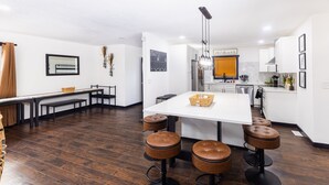 A modern kitchen with white cabinets, a central island with stools, and a dining area with a bench and table. - Flagship Park - 10 Mins to Everything! (Kansas City)