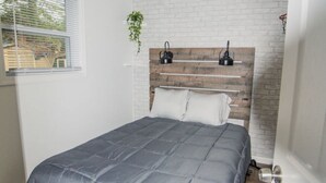 Un dormitorio con cama, ventilador de techo, pared de ladrillo decorativa y ventana con persianas.