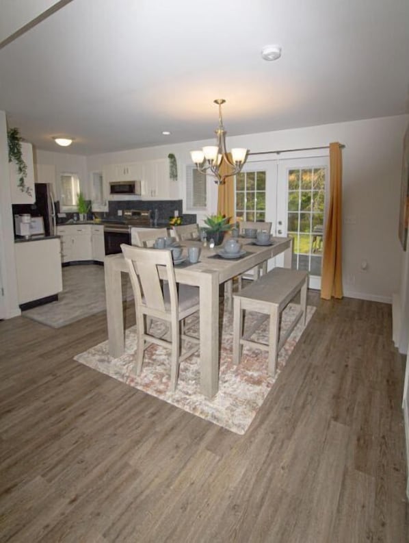 A modern kitchen with white cabinets, a dining area with a wooden table and chairs, and a chandelier.