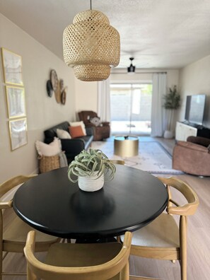 A dining area with a round black table, wooden chairs, a woven pendant light, and a potted plant. - The Hillside Hacienda located in the heart of Yuma. Hospital Nearby. (Yuma)
