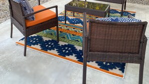 Zona salotto esterna con mobili in vimini e un tappeto decorato.