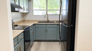 Una cucina compatta con mobili azzurri, un frigorifero nero e una finestra che lascia entrare luce naturale.