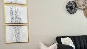Un soggiorno con un divano nero, un cesto in vimini con una coperta bianca e grigia, e tre opere d'arte incorniciate appese al muro.