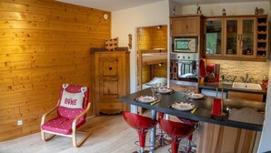Une cuisine chaleureuse aux murs en bois, une table à manger dressée pour quatre personnes et une chaise rouge agrémentée d’un coussin en forme de cœur.