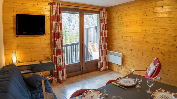 Une pièce chaleureuse avec un décor intérieur en bois, un canapé, une table dressée pour le repas et un téléviseur fixé au mur.