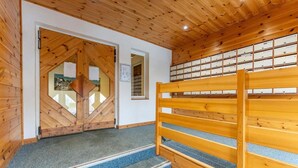 Un escalier en bois, avec un banc au sommet, mène à une pièce dotée d’une porte en bois et d’un mur recouvert de boîtes de rangement.