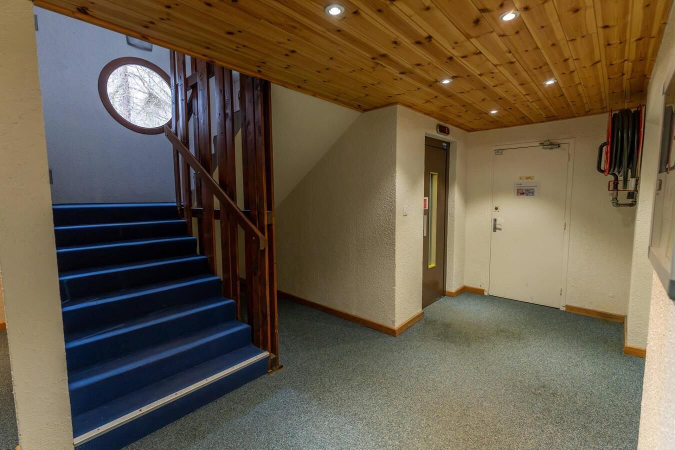 Una escalera con escalones azules que conduce a una plataforma, un techo de madera y una puerta con un letrero encima.