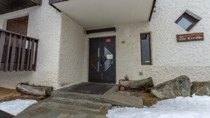 Une entrée d’immeuble avec une porte noire, des marches en pierre et une enseigne en bois sur laquelle on peut lire « Les Écrins ».