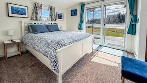 A bedroom with a bed, a nightstand, a window with curtains, and a view of a snowy landscape. - Peaceful Beachfront Cottage - Large Deck & Fire Pit - Gorgeous Views & Wildlife (Bremerton)