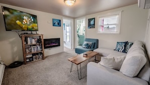 A living room with a flat-screen TV, a bookshelf, a blue sofa, and a coffee table. - Peaceful Beachfront Cottage - Large Deck & Fire Pit - Gorgeous Views & Wildlife (Bremerton)