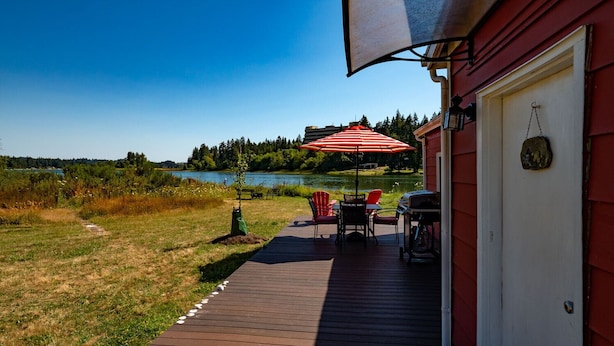 A deck with a red umbrella, a grill, and a chair. - Peaceful Beachfront Cottage - Large Deck & Fire Pit - Gorgeous Views & Wildlife (Bremerton)