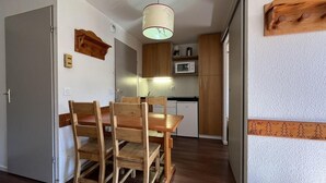 A compact kitchen with wooden cabinets, a microwave, and a dining area with a wooden table and chairs. - Ski-in/ski-out & foot of the slopes, 6th floor, balcony, tv, ski locker, 25m², La Plagne (La Plagne)