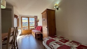 A bedroom with a bed, a wooden wardrobe, a desk, and a chair. There is a window with a view of buildings and hills. - Ski-in/ski-out & foot of the slopes, 6th floor, balcony, tv, ski locker, 25m², La Plagne (La Plagne)