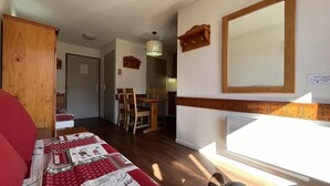 A cozy room with a wooden wardrobe, a red sofa, a dining table with chairs, and a mirror on the wall. - Ski-in/ski-out & foot of the slopes, 6th floor, balcony, tv, ski locker, 25m², La Plagne (La Plagne)