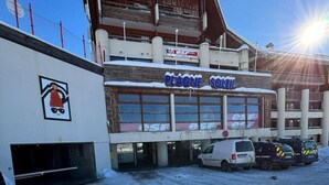 A building with a sign reading "PLAGNE SOLEIL" and a logo with a red hat and sunglasses. There are parked vehicles in front. - Ski-in/ski-out & foot of the slopes, 6th floor, balcony, tv, ski locker, 25m², La Plagne (La Plagne)